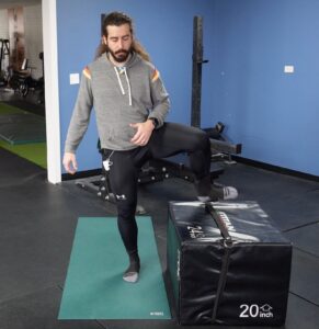 Dr. John lifting his left leg over the box to complete the leg circles exercise as part of his hip mobility routine